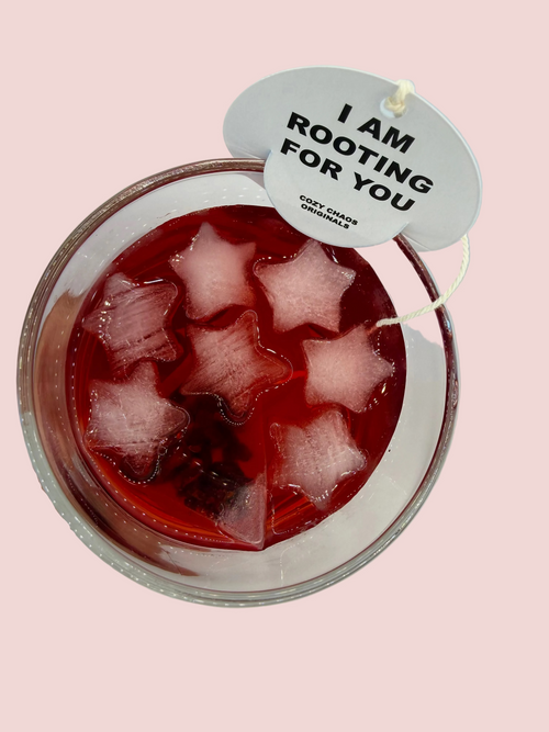 A glass cup filled with hibiscus tea and tea tag with quote "I AM ROOTING FOR YOU" sitting on the rim of the cup.